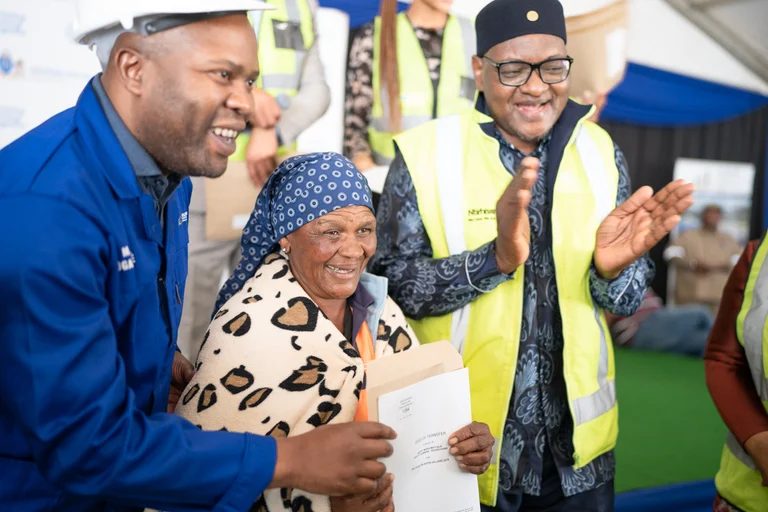 Officials applaud an elderly resident receiving her title deed at Affri-Village Greenhills